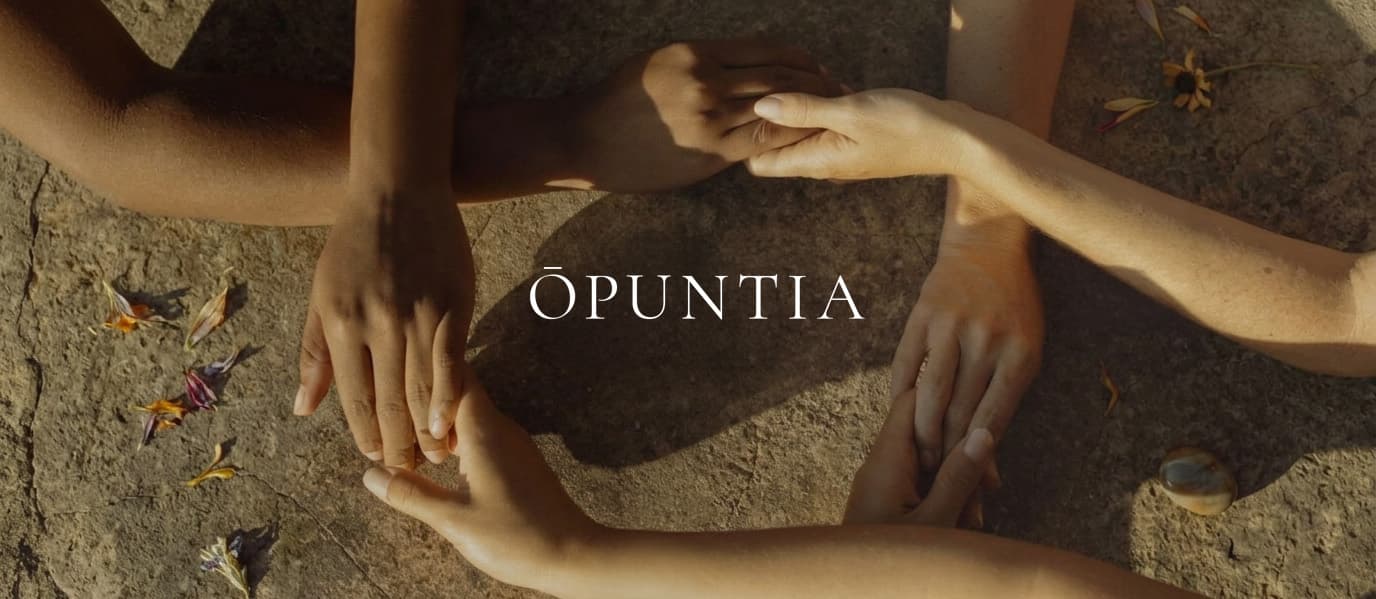Several pairs of joined hands resting together on sunlit stone, with the ŌPUNTIA wordmark at the centre.