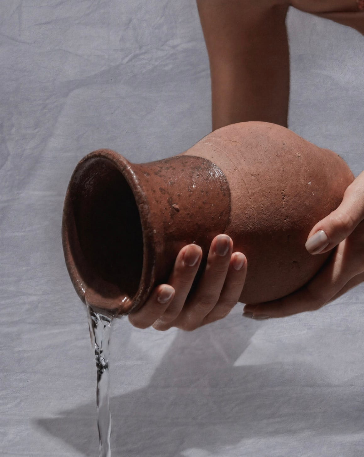 Hands pouring water from a handmade clay vessel over natural linen.